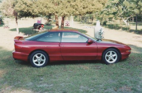 1994 Ford Probe - This red coupe is parked on a grassy area with trees and outdoor furniture visible.