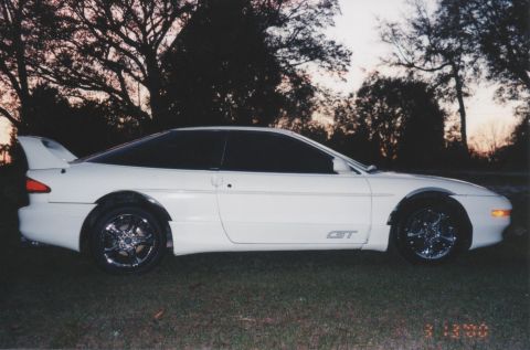 1994 Ford Probe - A white 1994 Ford Probe GT is shown from the side profile with a prominent rear spoiler and aftermarket wheels.