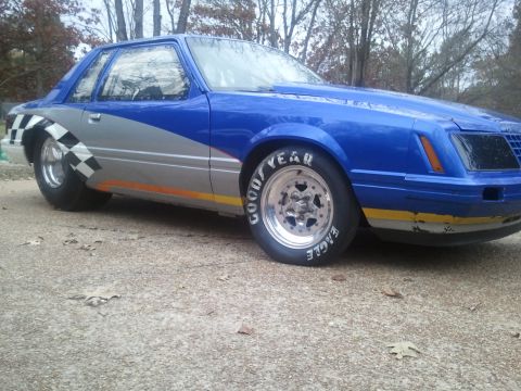 1967 Ford Mustang - A blue and silver drag car with a checkerboard fender flare is parked outdoors.