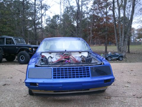 1967 Ford Mustang - Front view of a blue car with its hood open, parked outdoors next to a black Ford Bronco.