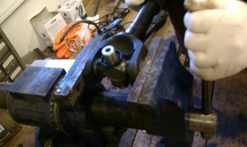 1979 Ford Bronco - A close-up view of a universal joint secured in a vise, with a gloved hand operating a tool.