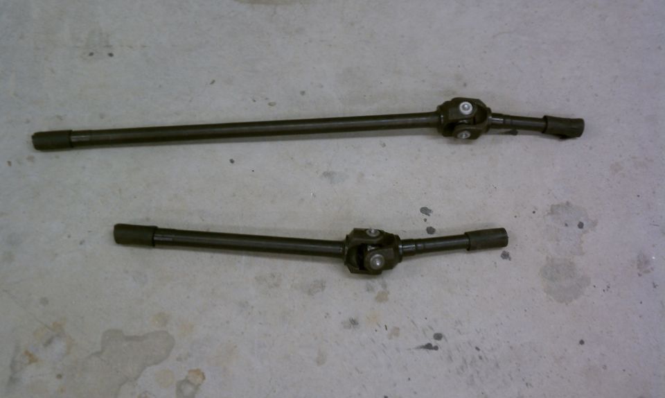 Two dark driveshafts with universal joints on a concrete floor