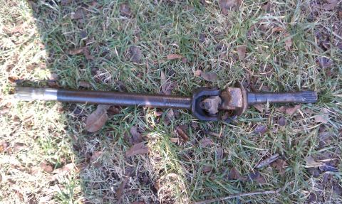 1979 Ford Bronco - A driveshaft with a universal joint is shown resting on a grassy surface.