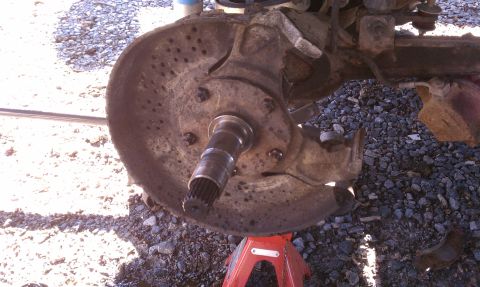 1979 Ford Bronco - Close-up of a heavily rusted brake rotor and hub assembly, supported by a red jack stand.