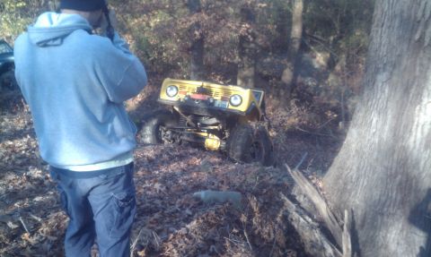1979 Ford Bronco - A yellow 1979 Ford Bronco is seen tilted off-road, with a person in the foreground filming the scene.