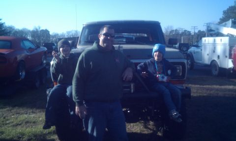 1979 Ford Bronco - Family poses with a 1979 Ford Bronco, with another vehicle on a trailer in the background.