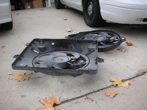 2004 Ford Crown Victoria - Two radiator fans are placed on the ground next to a white vehicle.