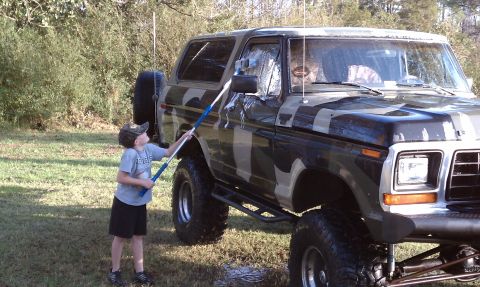 1979 Ford Bronco - A young boy washes a lifted, camouflage-painted Ford Bronco outside.