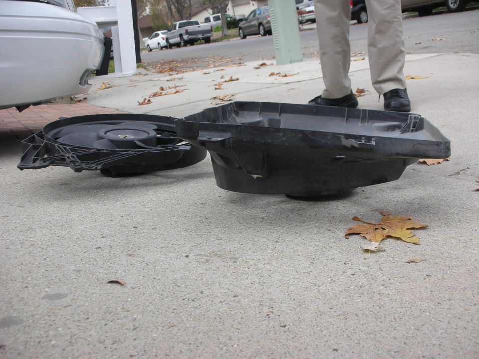 car fan and plastic shroud sitting on pavement next to a white car
