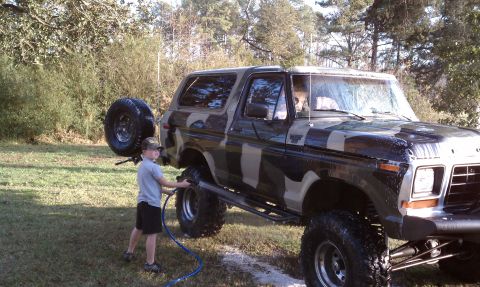 1979 Ford Bronco - A child washes a lifted, camouflage-painted 1979 Ford Bronco in a grassy yard.