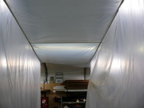 1976 Chevrolet Corvette - The interior of a temporary structure, possibly a paint booth or workshop, is covered in plastic sheeting, with a 'VISITOR PARKING ONLY' si…