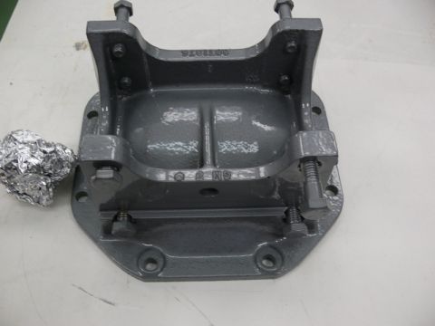 1976 Chevrolet Corvette - A gray metal bracket with bolts and a piece of foil is shown against a light-colored surface.