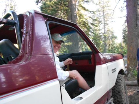 1991 Ford Bronco - A man smiles from the driver's seat of a red and white 1991 Ford Bronco, parked outdoors.