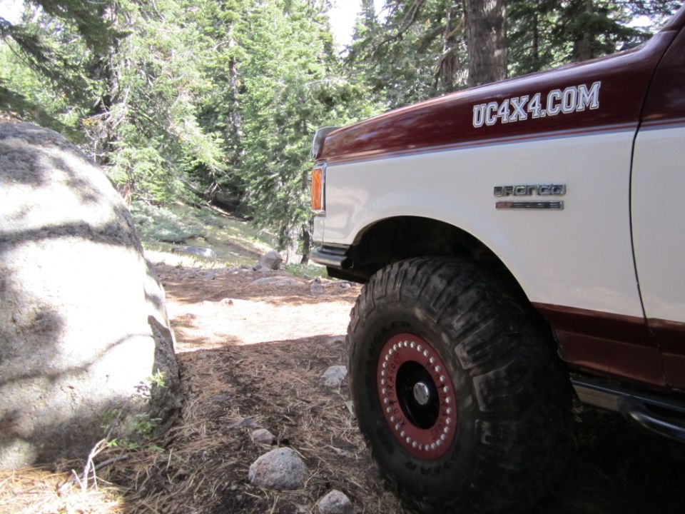 Side view of a 1991 Ford Bronco parked on a dirt trail with trees and a large rock