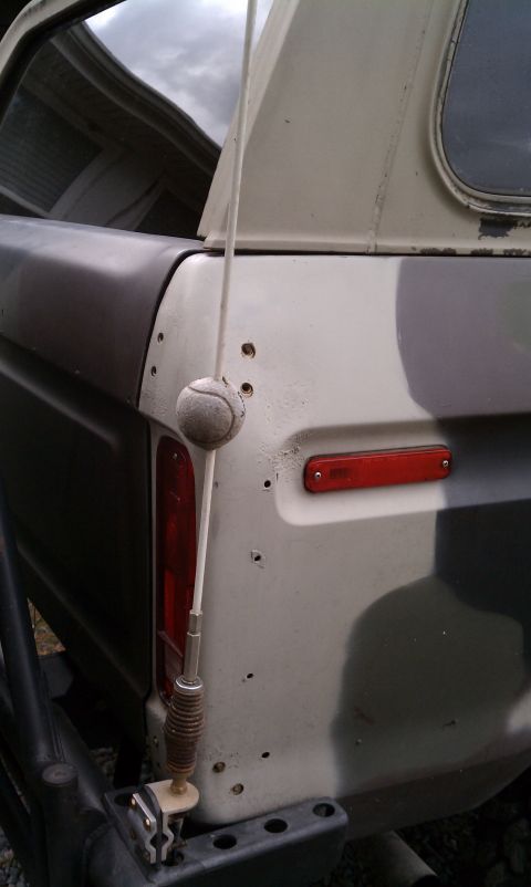 1979 Ford Bronco - The rear quarter panel of a camouflage SUV shows a red reflector and a tennis ball attached to the antenna.
