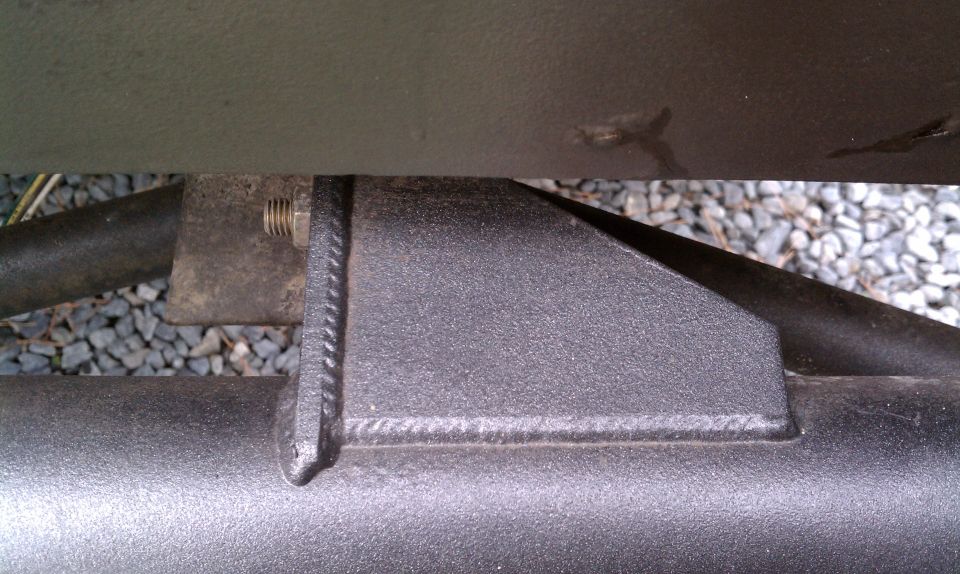 Close-up of a welded metal bracket attached to a tubular frame rail, with a bolt visible