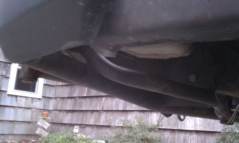 1979 Ford Bronco - The underside of a vehicle is shown, with a house and some greenery visible behind it.