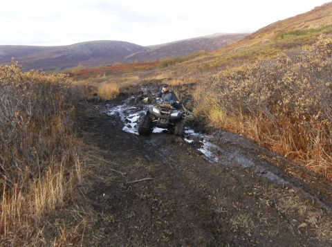 2000 Ford E350 - An ATV navigates a challenging muddy trail through a desolate, hilly landscape.