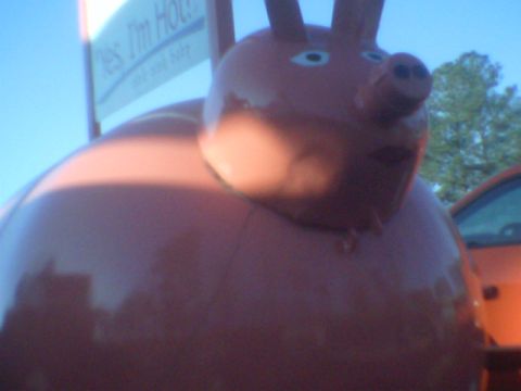 1979 Ford Bronco - A large, red pig sculpture with a cartoonish face stands in front of an orange vehicle.