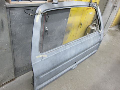 1987 Dodge 1500 - Unpainted vehicle door with window frame and wiring, in a workshop setting.