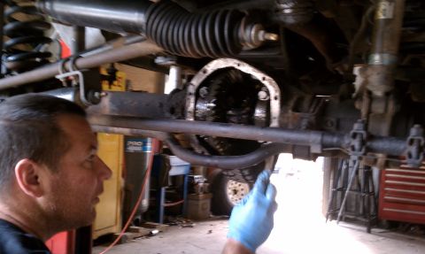 1979 Ford Bronco - A mechanic in blue gloves inspects the open differential of a vehicle, likely during a repair or maintenance procedure.