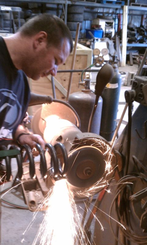 1979 Ford Bronco - A mechanic grinds a coil spring, creating a shower of sparks in a workshop environment.
