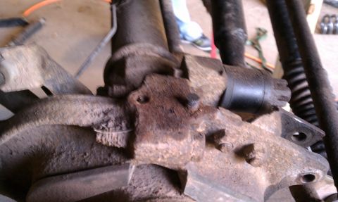 1979 Ford Bronco - Close-up view of a heavily rusted vehicle suspension part, showing bolts and brackets.