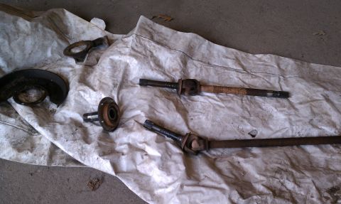 1979 Ford Bronco - Several automotive parts, including driveshafts and a brake rotor shield, are laid out on a white tarp.