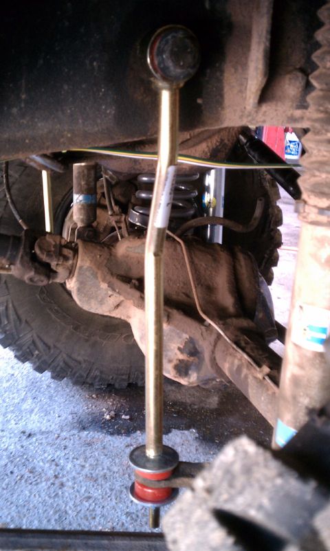 1979 Ford Bronco - Close-up of a sway bar end link with red bushings, part of a vehicle's suspension system.