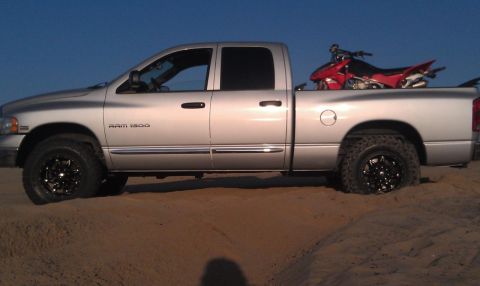 2005 Dodge 1500 - A silver Dodge Ram 1500 pickup truck is parked on sand with a red dirt bike loaded in its bed.