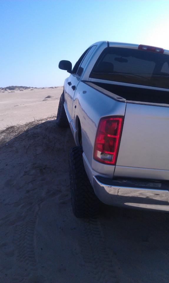 Silver pickup truck on a sandy dune under a clear blue sky