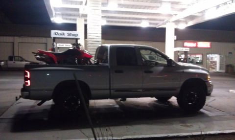 2005 Dodge 1500 - A silver pickup truck is parked at a gas station at night, with a red ATV loaded in the truck bed.