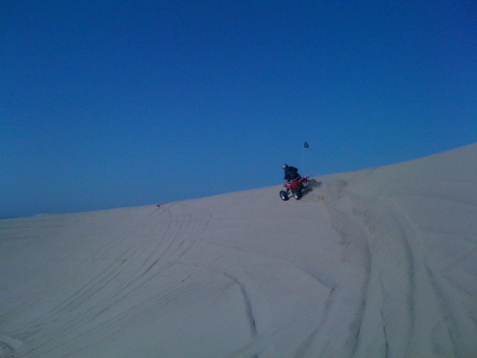 Red ATV with rider on a sand dune under a clear blue sky