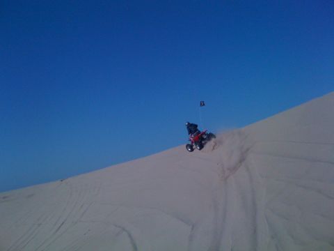 2005 Dodge 1500 - A quad bike rides down a sandy slope under a clear blue sky.