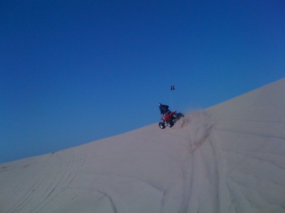 Red quad bike with rider on a sand dune, kicking up dust