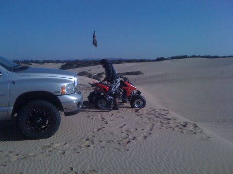 2005 Dodge 1500 - A silver pickup truck and a red ATV are parked on a sand dune under a clear blue sky.
