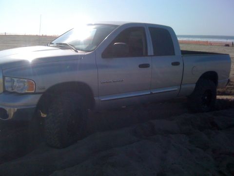 2005 Dodge 1500 - A silver Dodge Ram pickup truck is parked on a sandy beach with the ocean in the background.