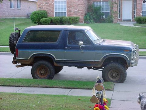 1986 Ford Bronco - This lifted Ford Bronco is parked in front of a brick house on a sunny day.