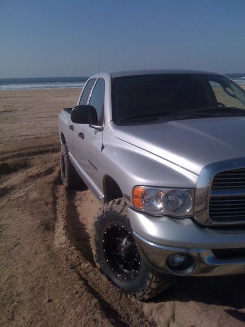 2005 Dodge 1500 - Silver pickup truck with aftermarket wheels on a sandy beach, ocean in background.