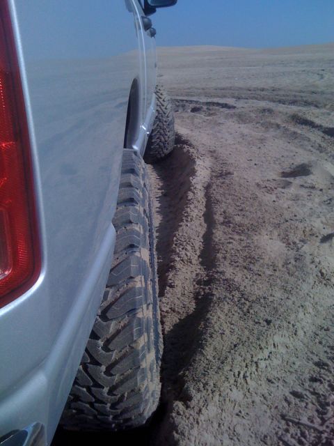 2005 Dodge 1500 - A silver pickup truck navigates sandy terrain, showing its side profile and aggressive tires.
