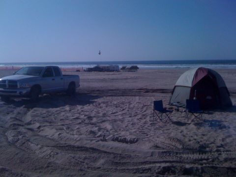 2005 Dodge 1500 - A silver Dodge Ram pickup truck is parked on a sandy beach next to a tent with the ocean in the background.