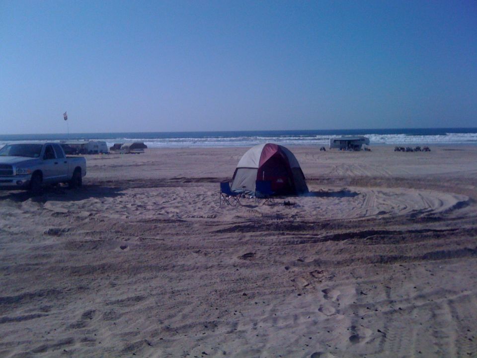 Silver pickup truck parked on a sandy beach near a tent and the ocean