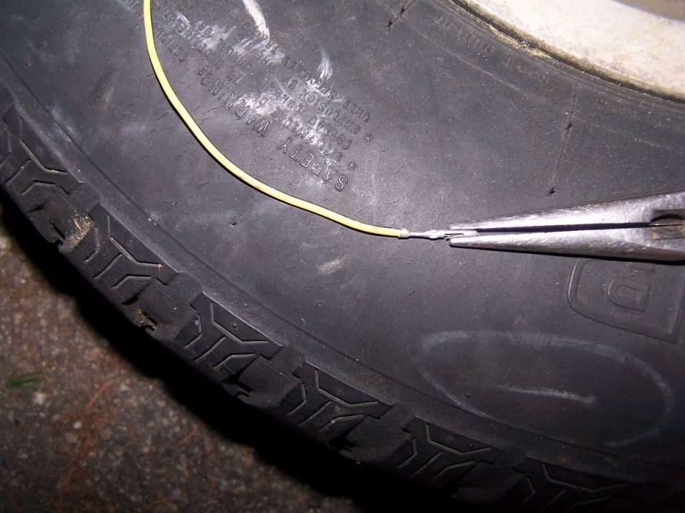 Tire sidewall with yellow wire being crimped by needle-nose pliers