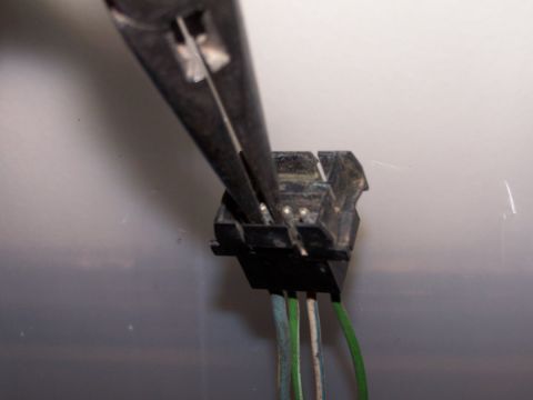 1973 Ford Bronco - Close-up of a vehicle's wiring harness connector being worked on with pliers.