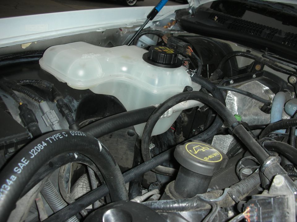 Engine bay with coolant reservoir and hoses visible. Some text on a hose reads "SAE J2064 TYPE C 0323A"