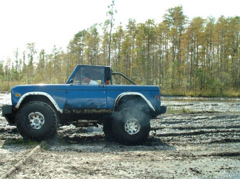 1992 Ford Bronco - A blue 1978 Ford Bronco navigates a muddy terrain with large tires.