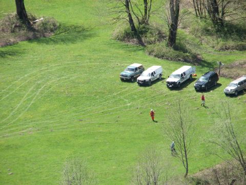 1990 Ford Bronco - A collection of vehicles are parked on a green, grassy hillside with trees in the background.
