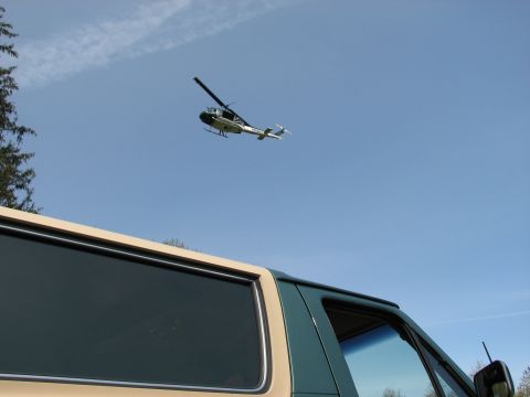 1990 Ford Bronco - A helicopter is seen in the sky above a two-tone tan and green vehicle, possibly a van or SUV.