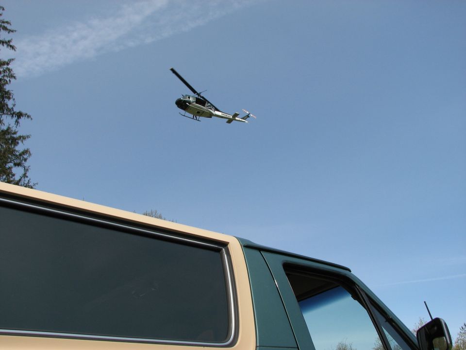 Helicopter flying in blue sky above a tan and green vehicle