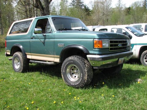 1990 Ford Bronco - This green Ford Bronco is parked on a grassy field with trees in the background.